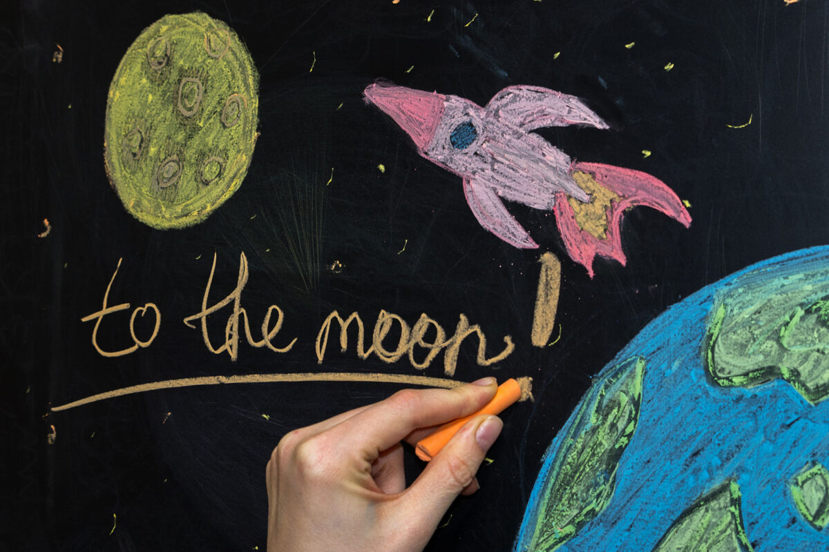 A chalkboard with "to the moon!" written on it next to a rocket, the Earth, and the Sun