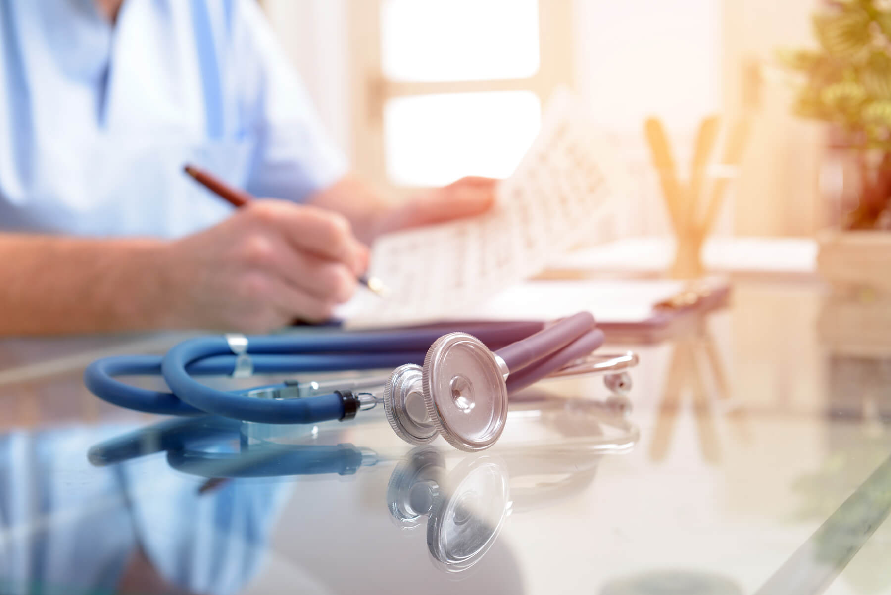 This image shows a stethoscope on a desk in front of a healthcare professional.