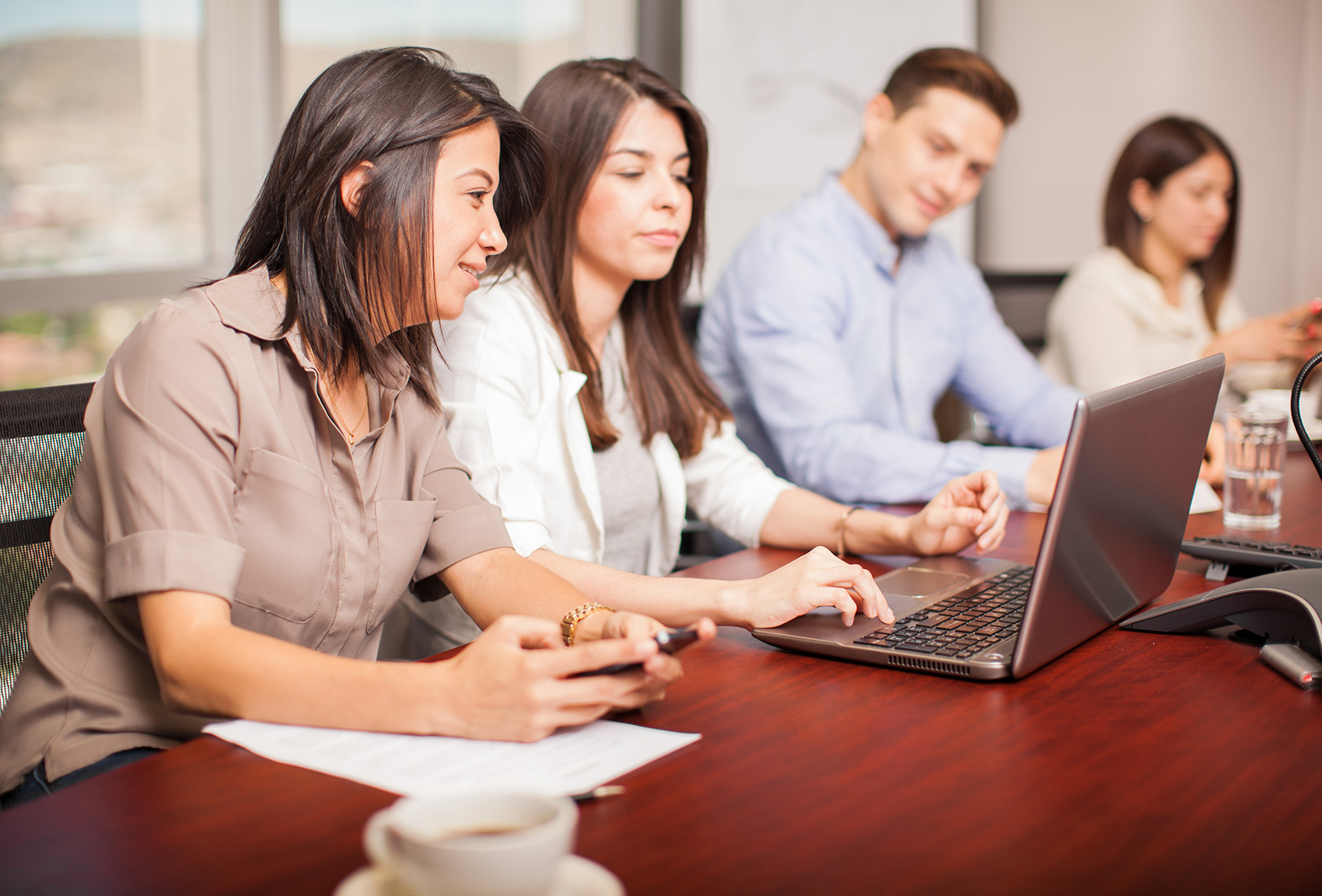 A few people look at a laptop screen in an office setting.